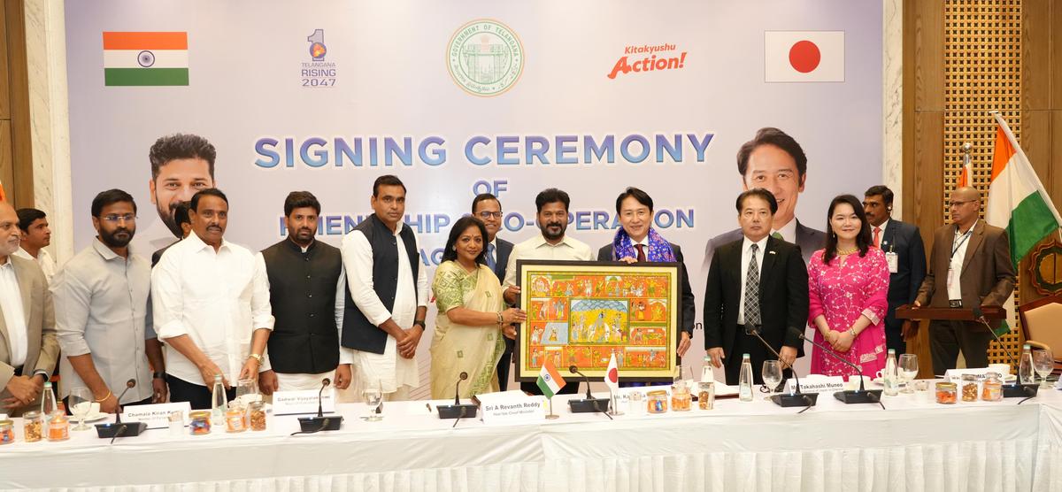 India-Japan officials at a formal signing ceremony for friendship and cooperation between Telangana and Kitakyushu, with dignitaries exchanging a traditional artwork.