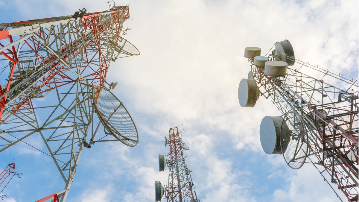 Low-angle view of multiple telecommunications towers with antennas and satellite dishes under a partly cloudy sky, symbolizing modern wireless communication infrastructure.
