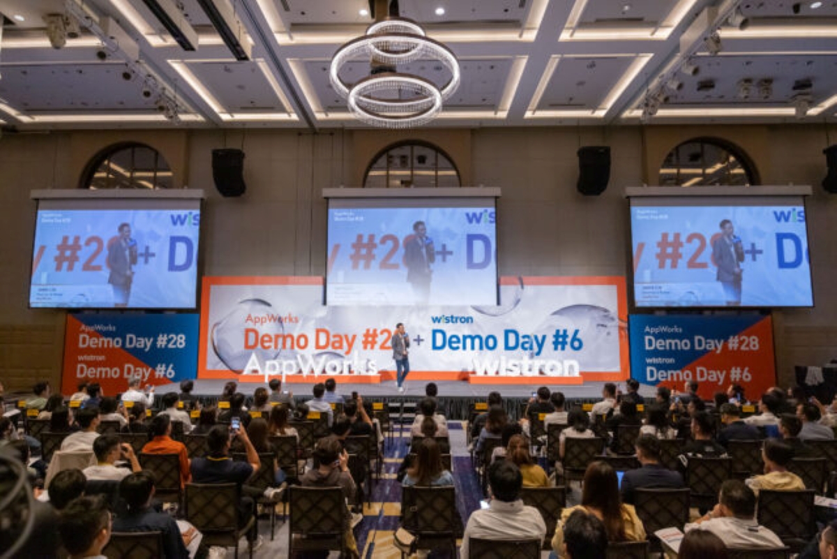 Speaker presenting on stage at AppWorks Demo Day #28 and Wistron Demo Day #6, with a large audience seated in a conference hall and presentation screens displaying event visuals.