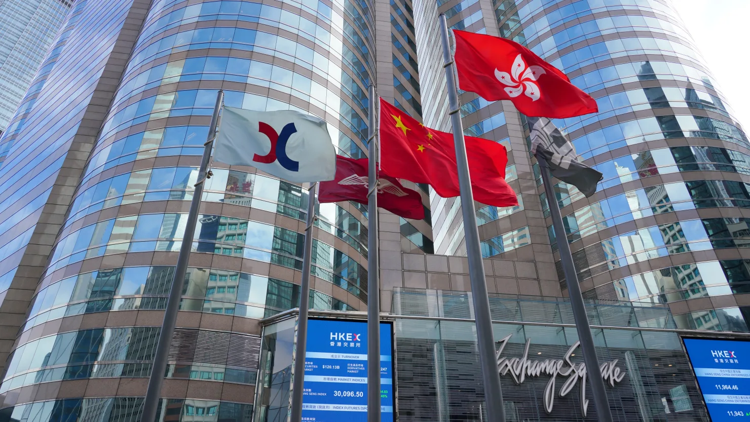 The Chinese and Hong Kong flags flutter as screens display the Hang Seng Index outside the Exchange Square complex, which houses the Hong Kong Stock Exchange