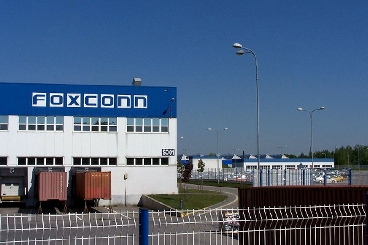 Photo by Foxconn manufacturing facility exterior with loading docks and cargo containers under a clear blue sky.