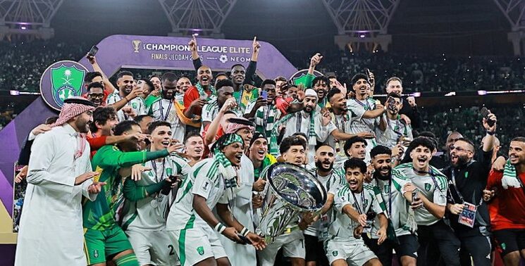 Saudi Arabian football team celebrating championship victory at the Champions League Elite Finals in Jeddah, holding the trophy on stage surrounded by cheering teammates and fans.