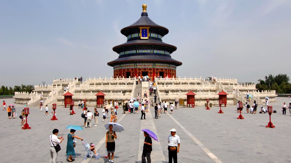 Tourists visiting the iconic Temple of Heaven in Beijing, China, on a sunny day with clear skies and traditional Chinese architecture.