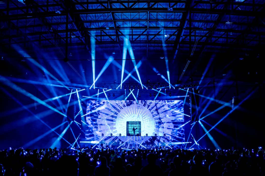 Ado World Tour 2025 concert in Bangkok featuring dramatic blue lighting, digital stage visuals, and a packed crowd with glow wristbands.