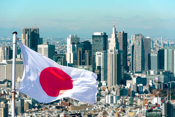 Japanese national flag waving above Tokyo city skyline with modern skyscrapers under a clear blue sky