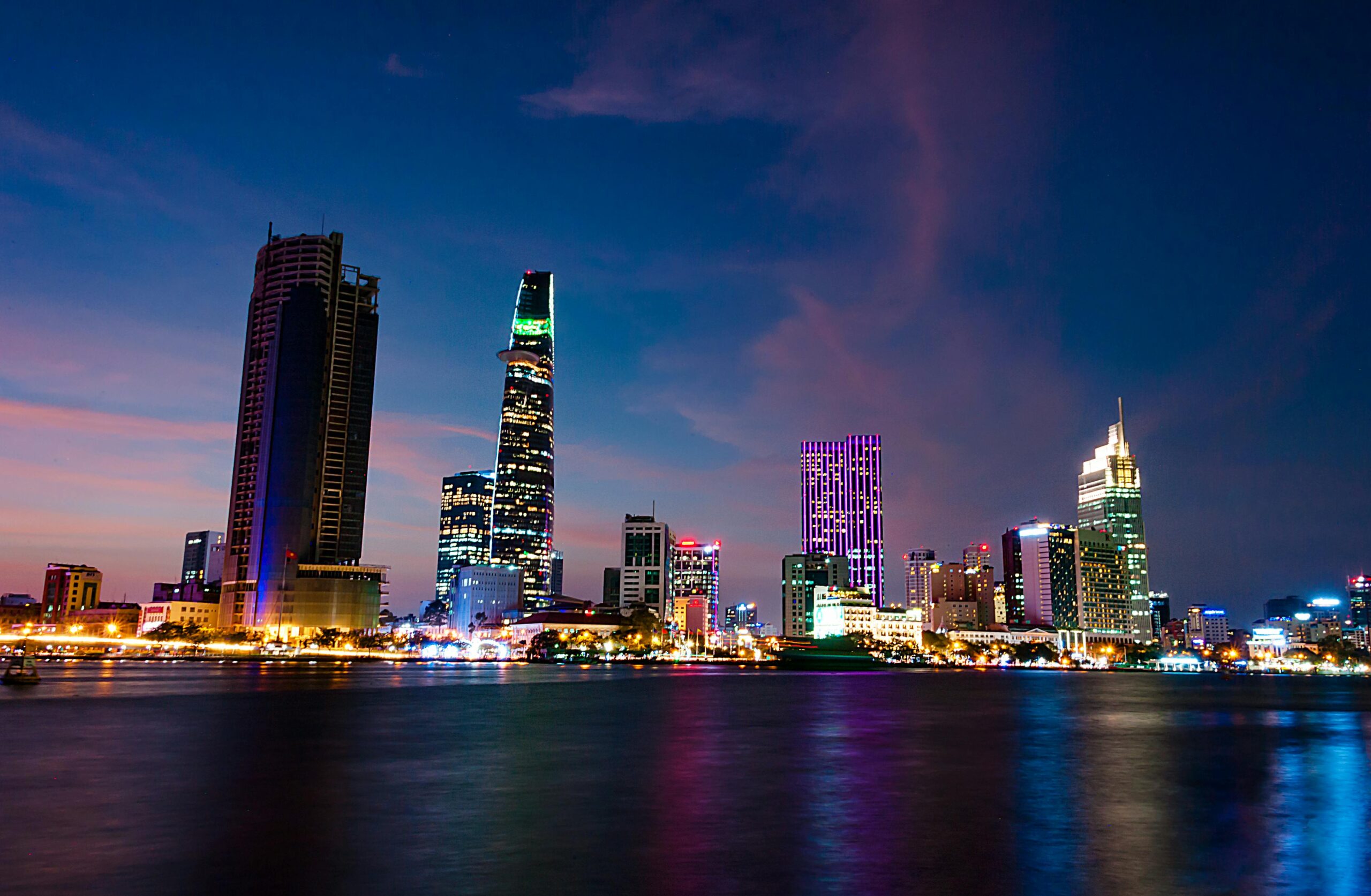 Night view of Ho Chi Minh City skyline in Vietnam with Bitexco Financial Tower and vibrant city lights reflecting on the Saigon River.