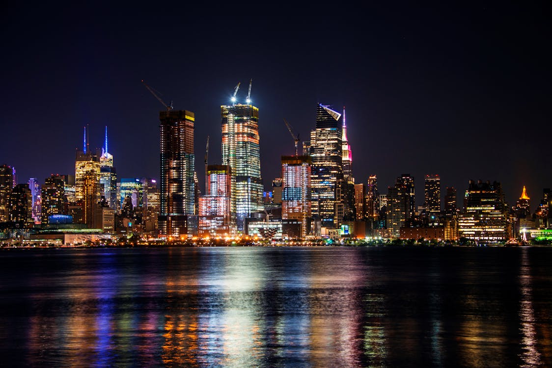 Vibrant New York City skyline at night with illuminated skyscrapers reflecting on the Hudson River"