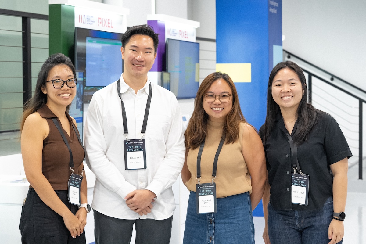 Group photo of four young professionals at The Work Revolution event, wearing name badges and smiling at the camera inside the PIXEL innovation hub