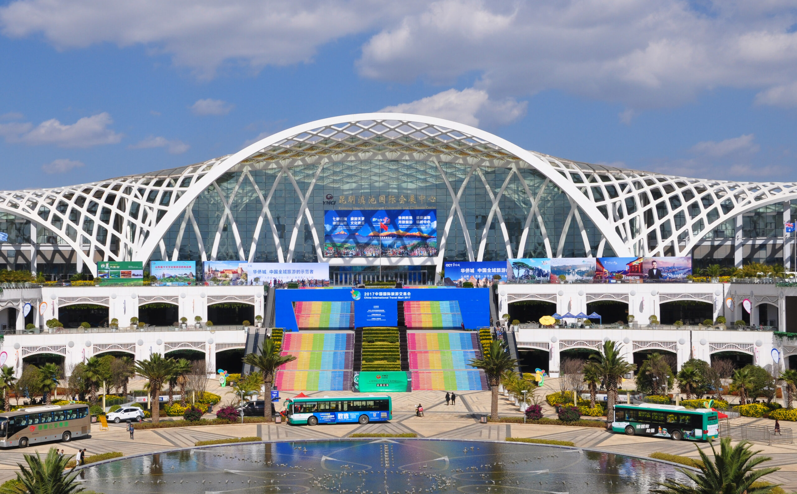 Kunming Dianchi International Convention and Exhibition Center with a colorful staircase and modern lattice-style architecture under a blue sky.