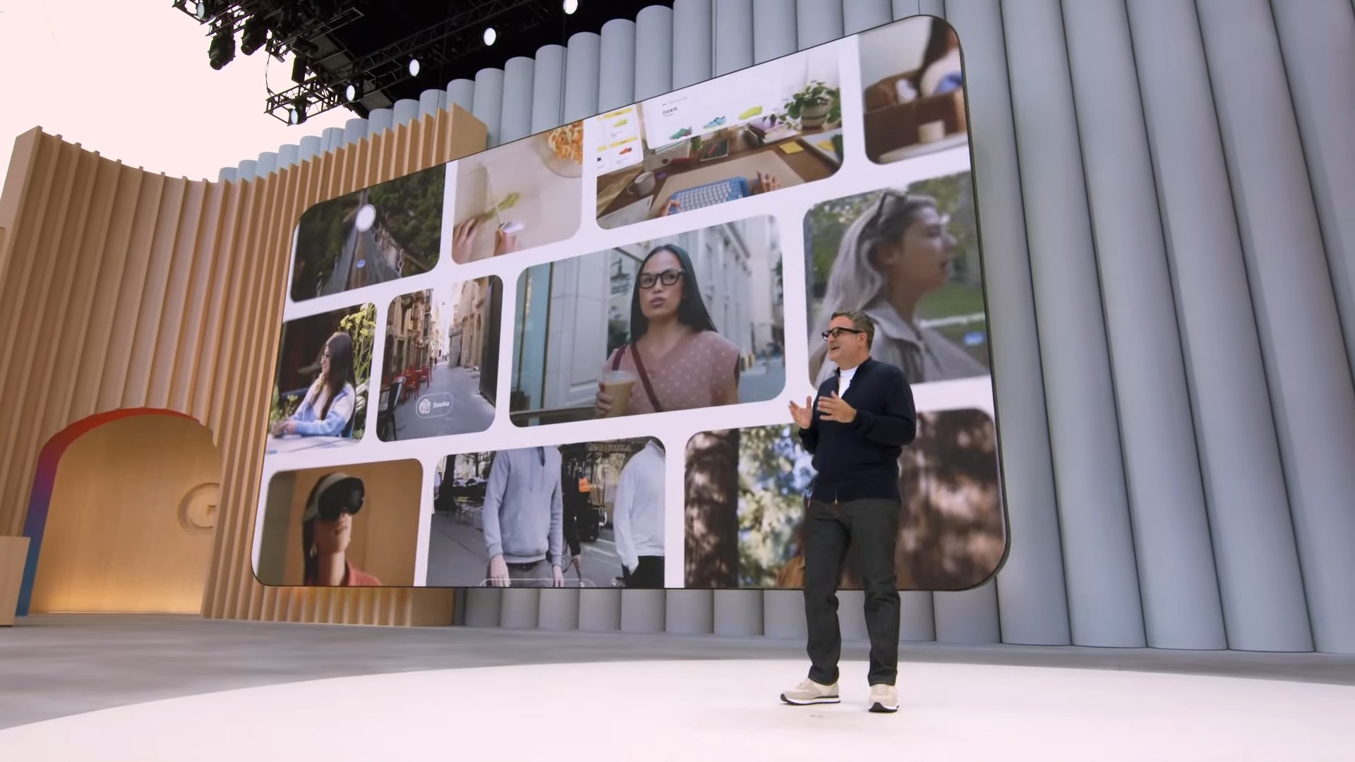 Speaker presenting on stage at a Google event with a large digital screen behind displaying lifestyle and tech-related visuals, symbolizing innovation and user-centric technology.