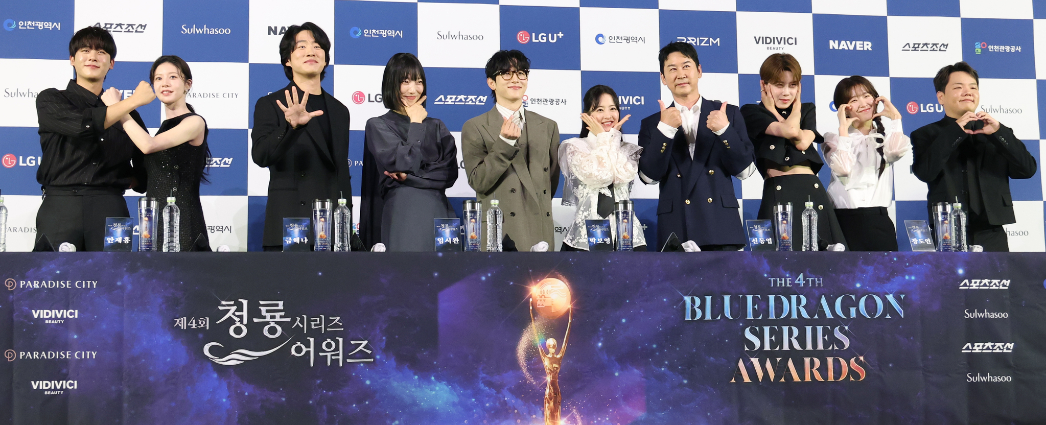 Cast members and celebrities pose at a press conference for the 4th Blue Dragon Series Awards, standing in front of a sponsor backdrop and event banner.