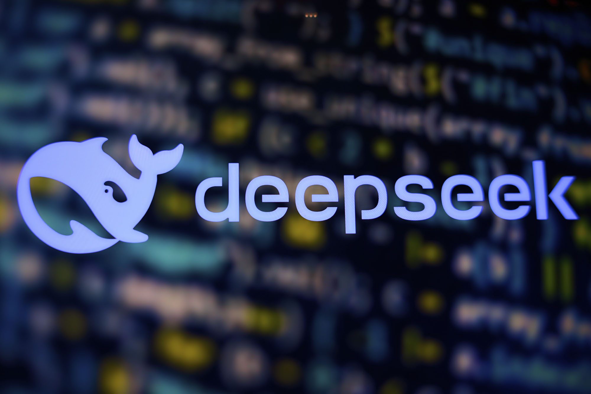 The logo of DeepSeek, featuring a stylized white whale encircling a dot (resembling an eye or a data point), next to the word "deepseek" in clean, modern lowercase font. The background is blurred, showing colorful lines of code, symbolizing the company’s focus on AI, data, or software development.
