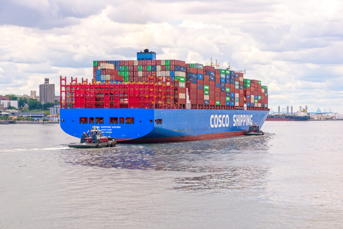 COSCO Shipping container vessel Sakura transporting stacked cargo containers across a major international waterway, illustrating global maritime trade and Chinese logistics operations.