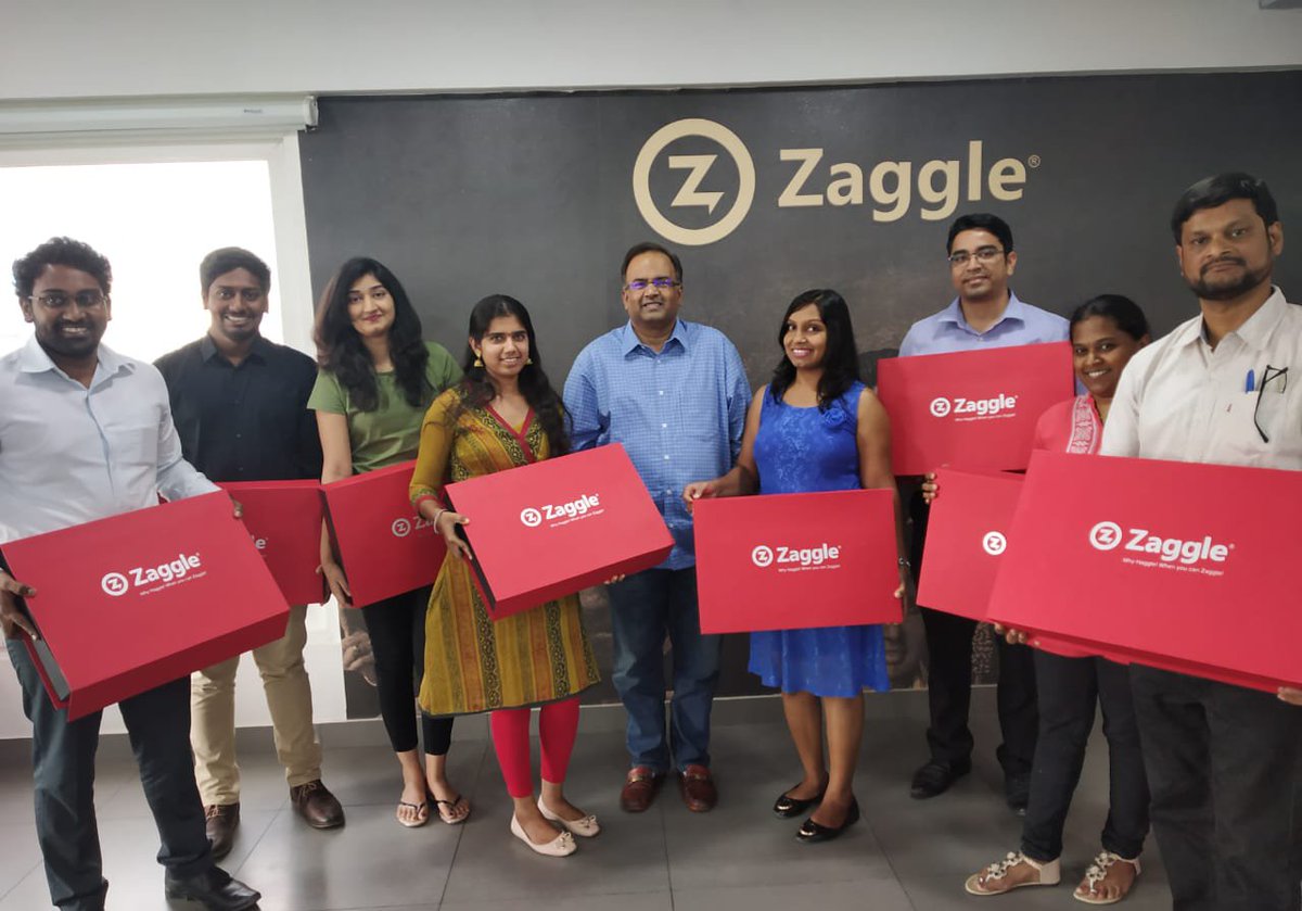 Zaggle employees posing with branded red gift boxes in front of the company logo wall, celebrating a team milestone or corporate event.