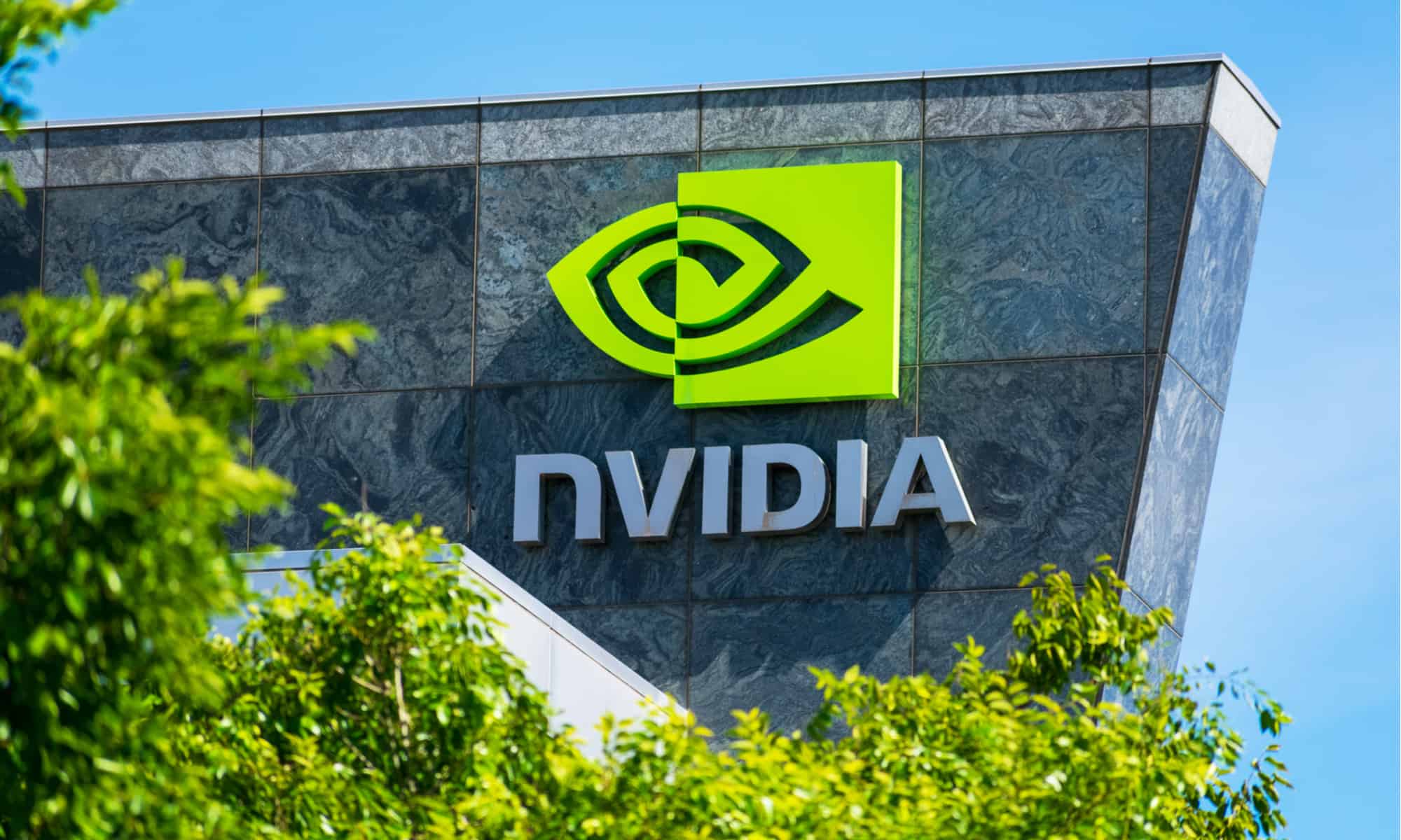 NVIDIA headquarters building with the company’s green eye logo and name displayed on a marble facade, framed by trees under a clear blue sky.