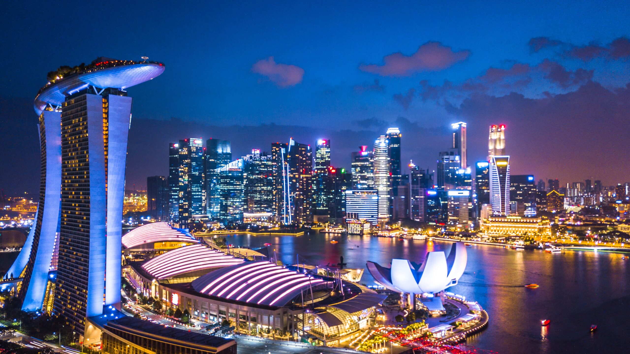 Singapore Marina Bay skyline at night, featuring Marina Bay Sands, the ArtScience Museum, and illuminated skyscrapers reflecting on the waterfront.