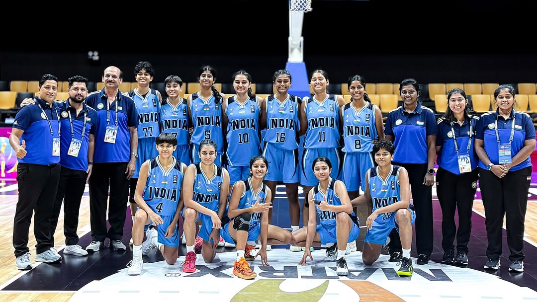 Indian women’s basketball team posing on court with coaches and staff during international championship.