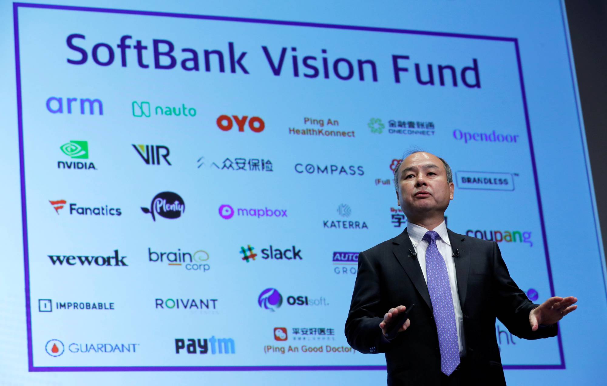 SoftBank Vision Fund presentation with Masayoshi Son speaking on stage in front of a screen displaying portfolio company logos including Arm, NVIDIA, Paytm, WeWork, Slack, and Coupang.