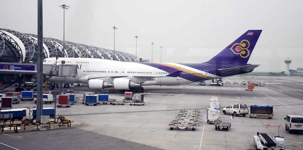Thai Airways Boeing 747 aircraft parked at Suvarnabhumi Airport in Bangkok, Thailand, with ground service vehicles and luggage carts in operation.