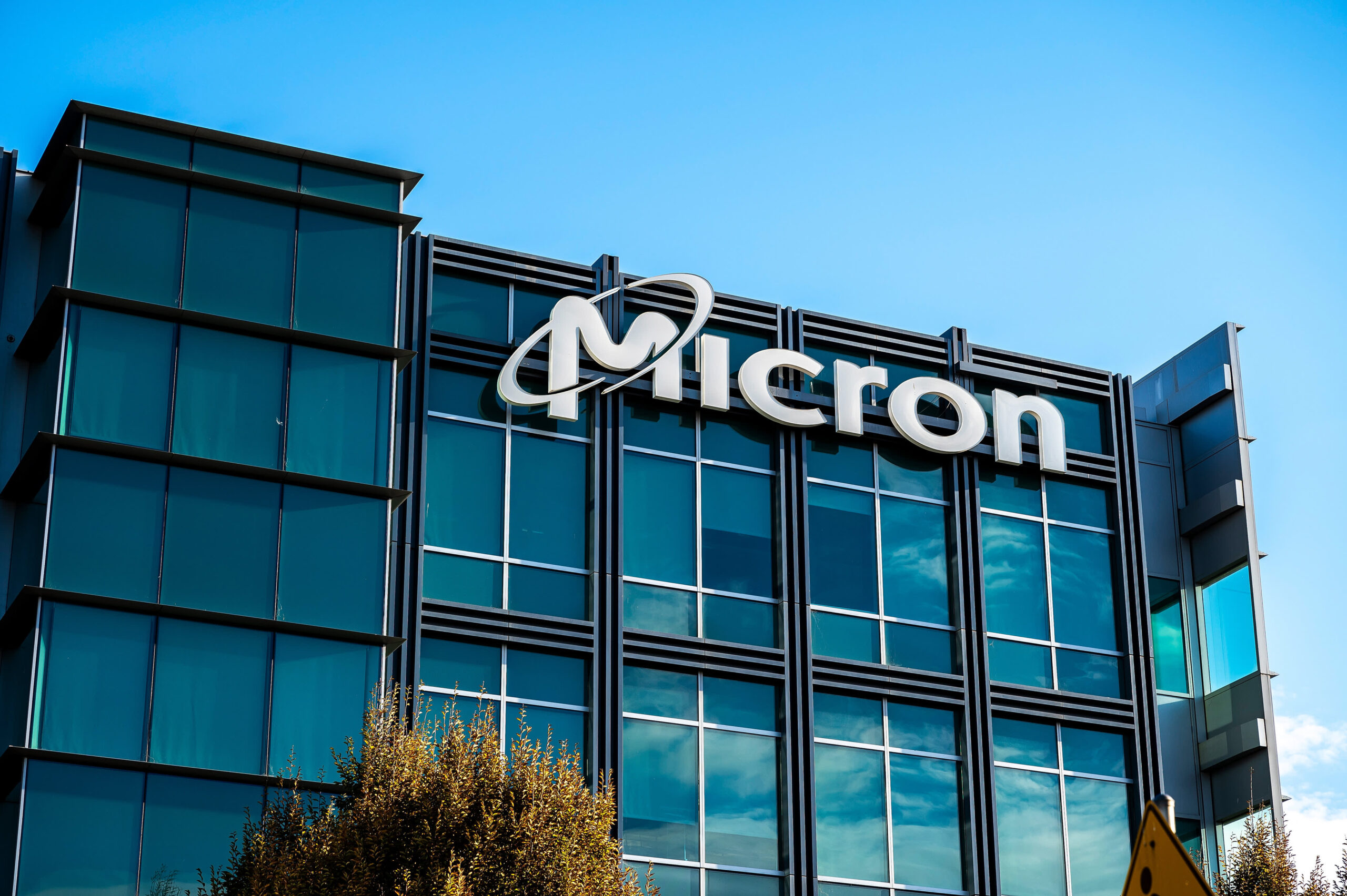Micron Technology corporate headquarters with glass facade and company logo displayed on building exterior under clear blue sky.