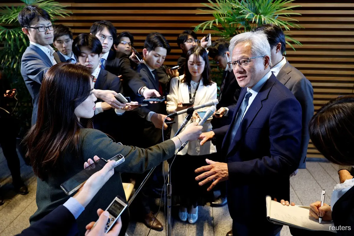 A senior business leader speaking to a large group of reporters holding microphones and recording devices during a press briefing in Japan.