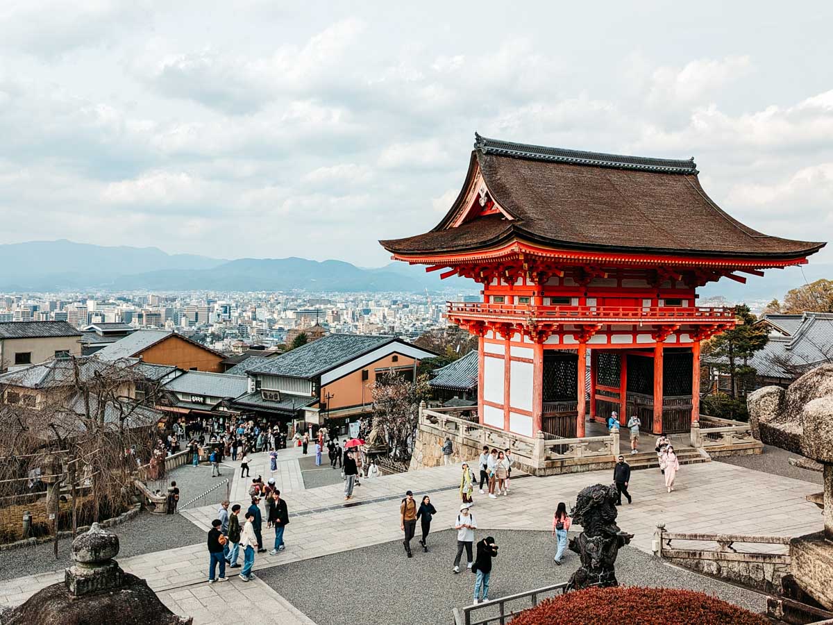 Tourists visiting Kiyomizu-dera Temple in Kyoto, Japan, with panoramic city views and traditional Japanese architecture.