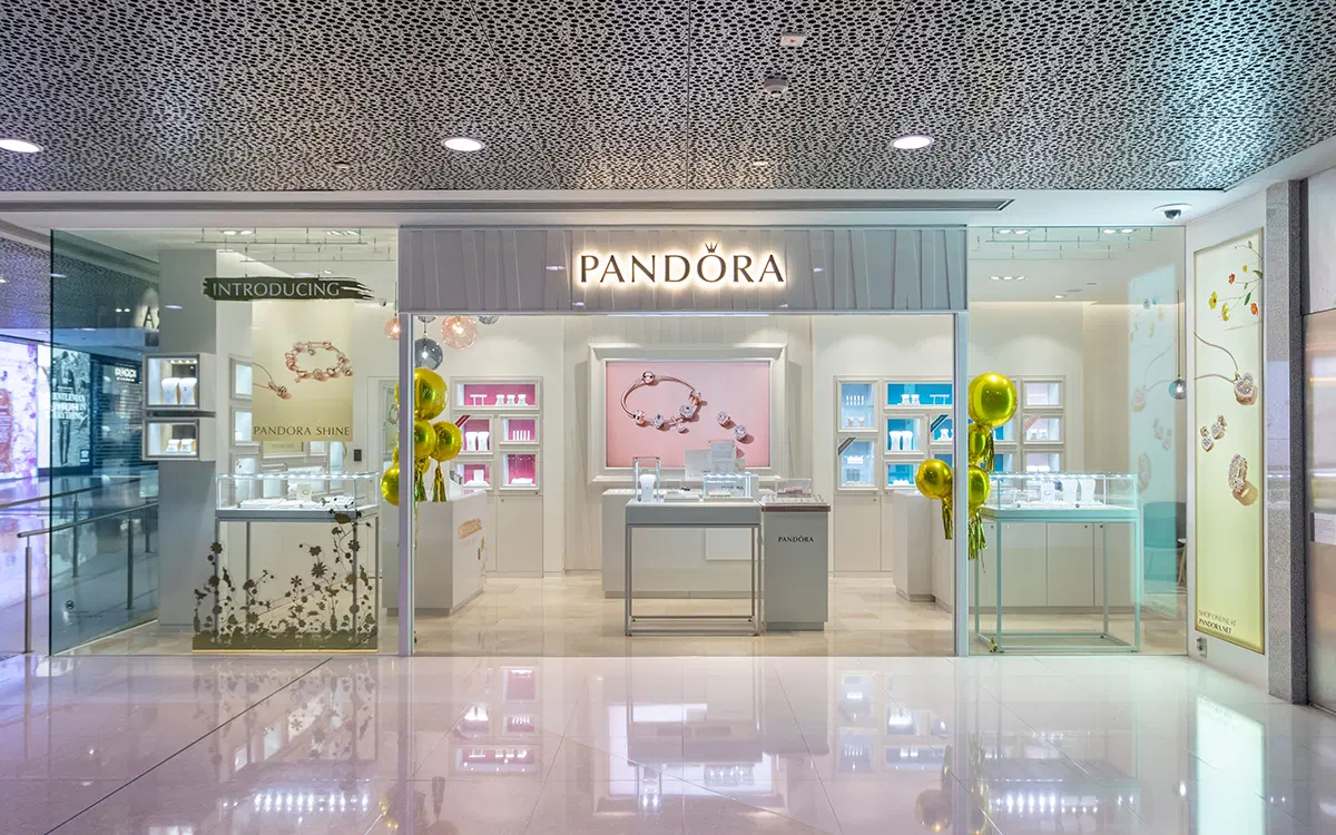 Front view of a Pandora jewelry store with elegant glass displays, showcasing bracelets, charms, and accessories under bright lighting in a modern shopping mall.