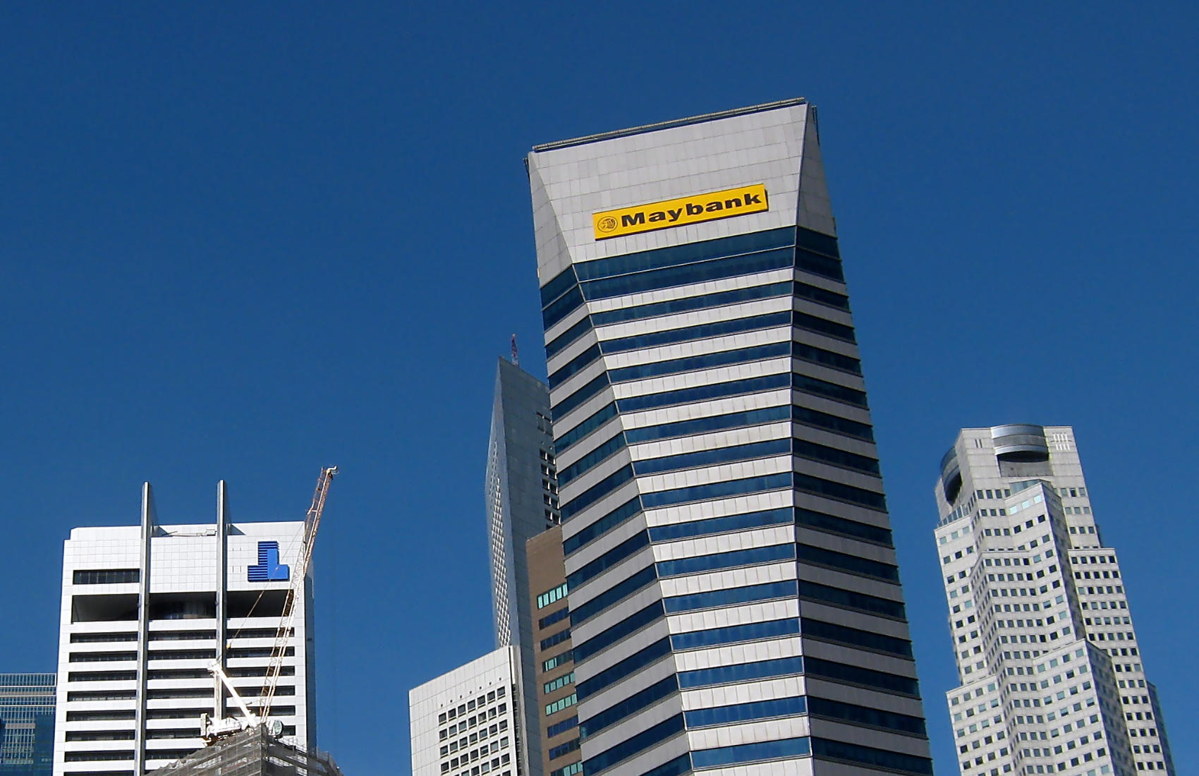 Maybank Tower skyscraper in Singapore’s financial district with its signature yellow logo, surrounded by other modern office buildings under a clear blue sky.