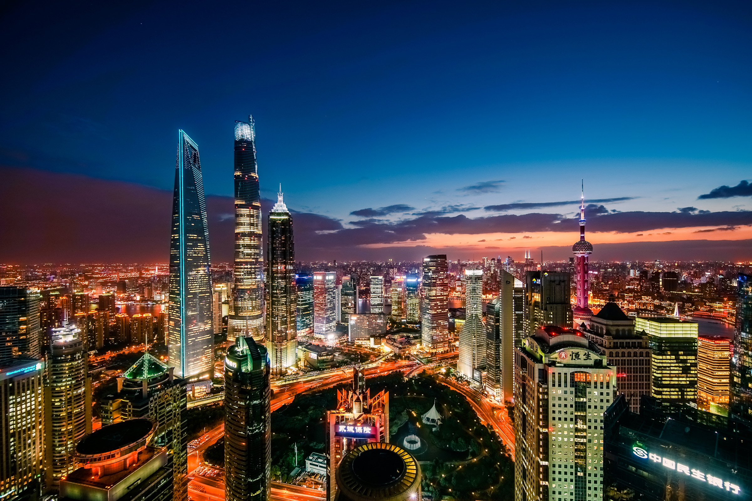 Shanghai skyline at dusk featuring Lujiazui Pudong skyscrapers, including Shanghai Tower and Oriental Pearl Tower, with city lights over the Huangpu River.