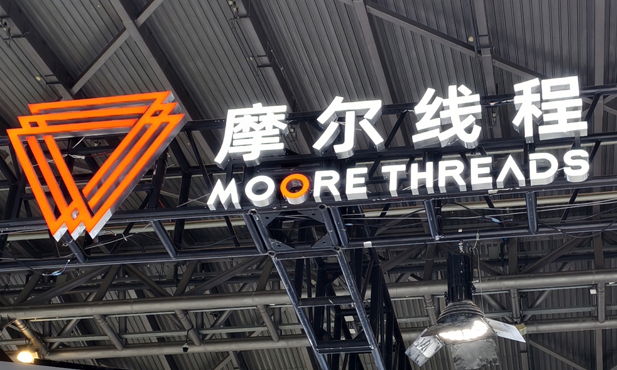 Moore Threads (摩尔线程) logo and bilingual company sign lit in white and orange on an industrial ceiling truss at a tech exhibition booth.
