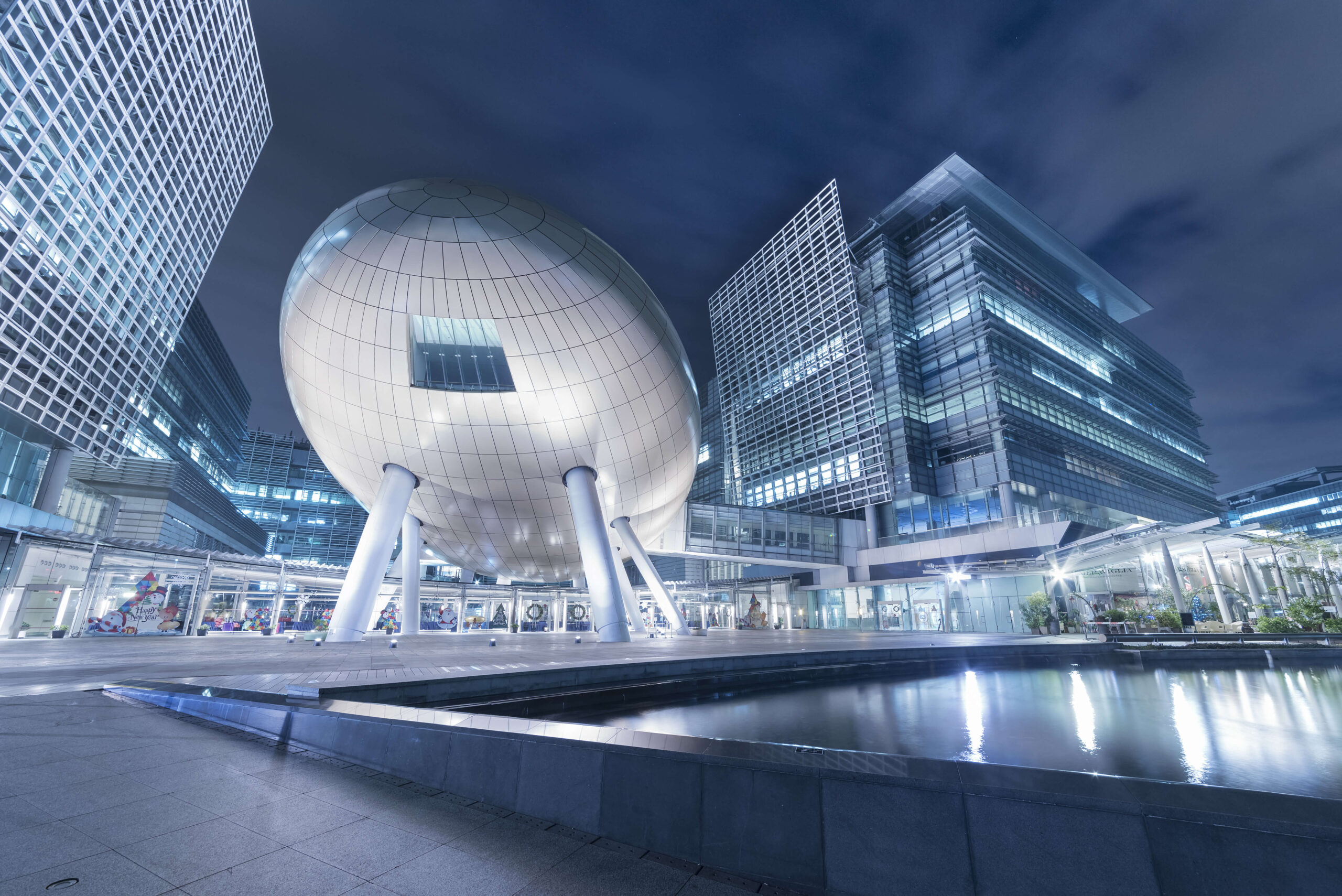 Night view of Oasis 21 in Nagoya, Japan, featuring the futuristic glass-and-steel spherical structure surrounded by modern office towers and illuminated urban architecture.