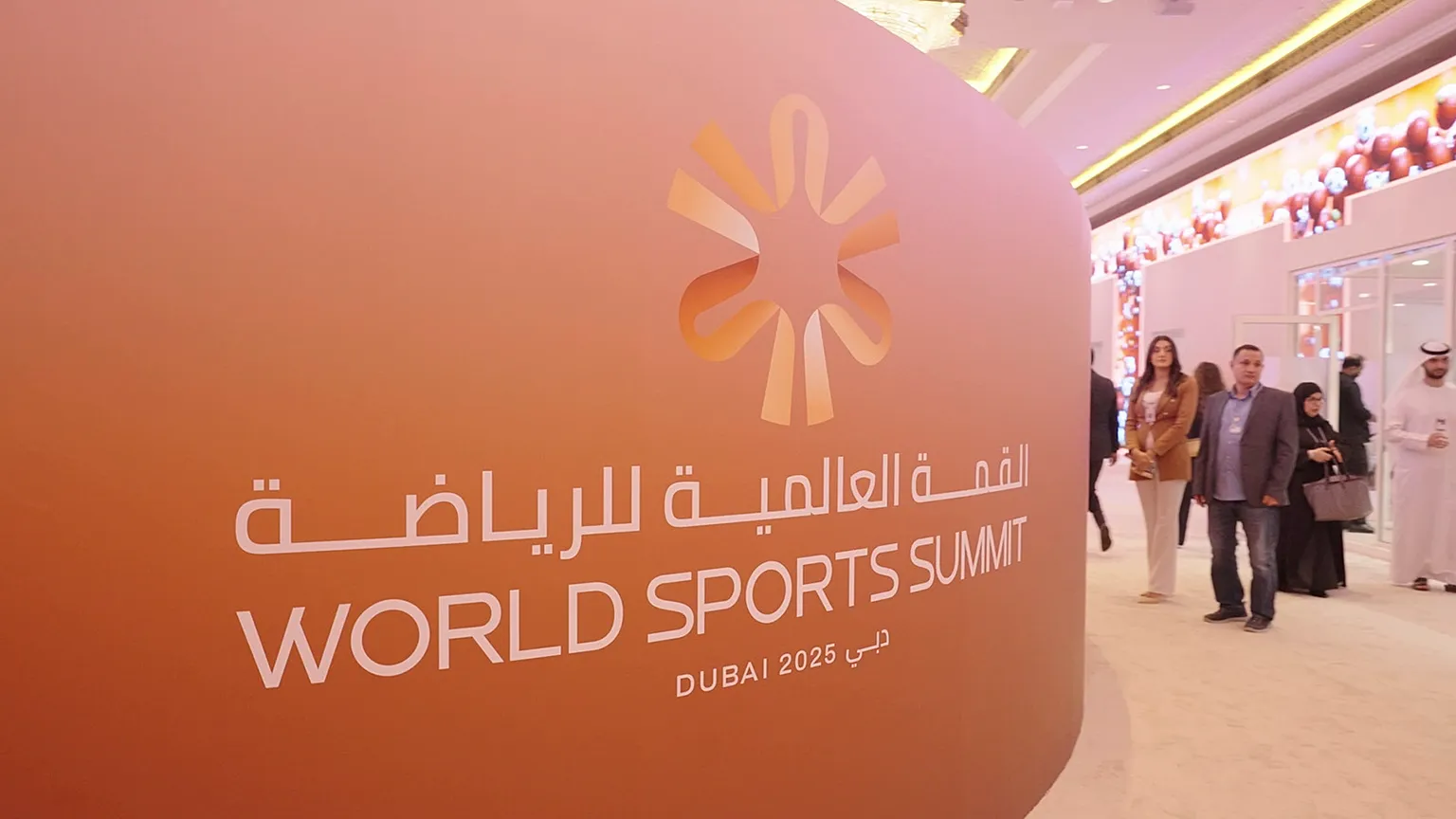 World Sports Summit Dubai 2025 event signage with Arabic and English branding at the exhibition venue, as attendees walk through the conference hall.