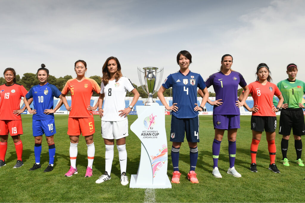 Captains from multiple national women’s football teams stand alongside the AFC Women’s Asian Cup trophy before a match, representing Asia’s leading teams and highlighting the growth of women’s football across the region.