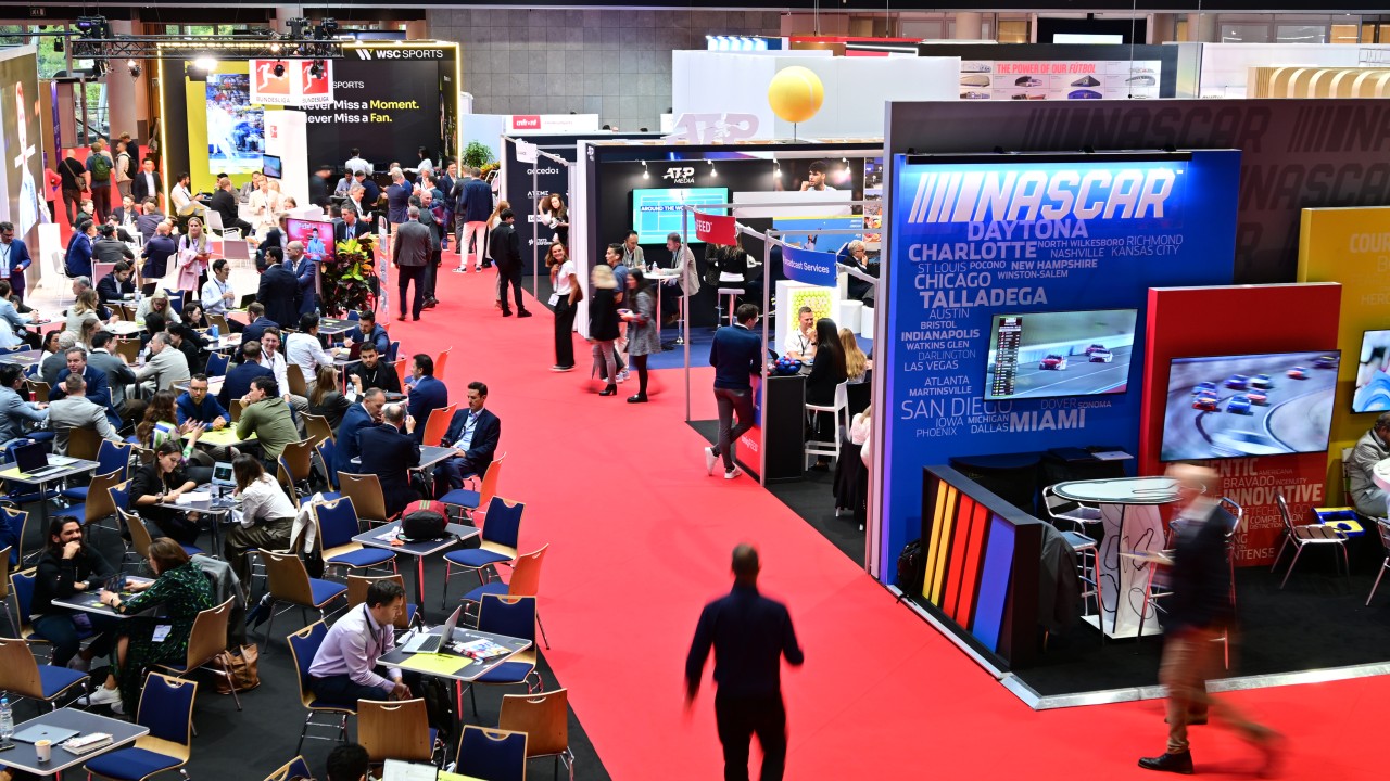 Global sports and media trade show exhibition floor featuring NASCAR and ATP Media booths, with business networking sessions and industry professionals.