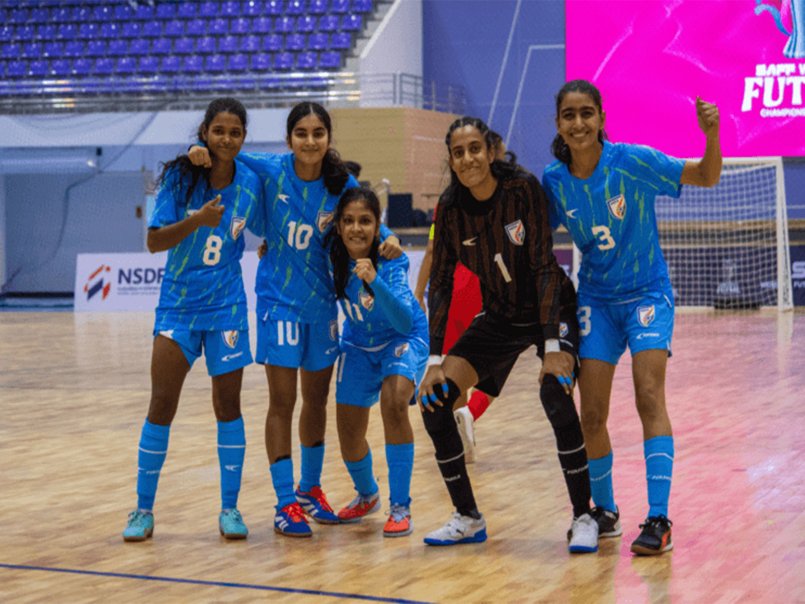 India women’s futsal team players posing together on indoor court during international tournament, wearing blue national jerseys.
