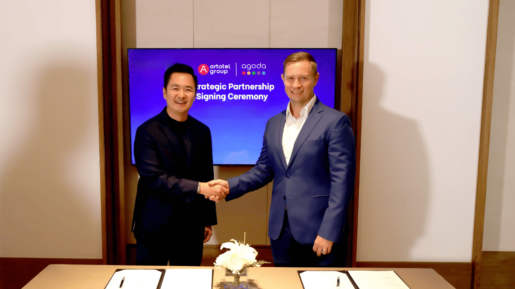 Artotel Group and Agoda executives shake hands during strategic partnership signing ceremony, highlighting hospitality and online travel collaboration.
