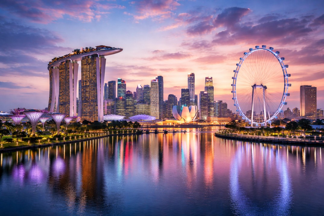 Singapore skyline at sunset featuring Marina Bay Sands, Singapore Flyer, and illuminated cityscape reflected in Marina Bay waters.
