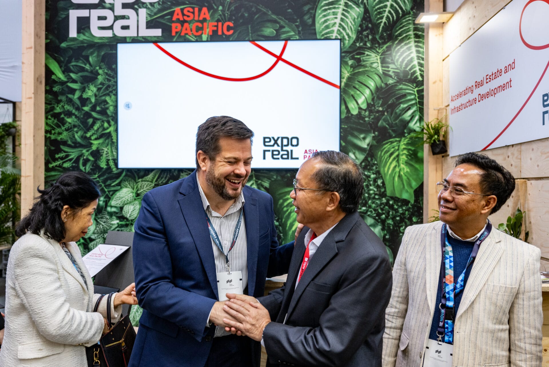 Business leaders shaking hands at Expo Real Asia Pacific event booth focused on real estate and infrastructure development networking.